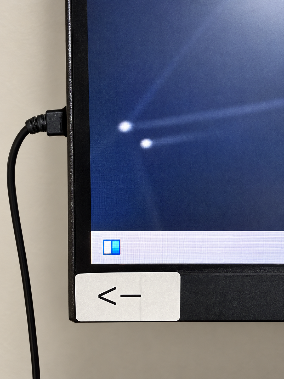 HitTrax monitor edge and arrow marking the power-button location